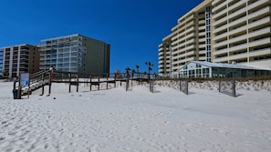 A beachfront hotel with multiple floors, a wooden walkway, and a glass building.