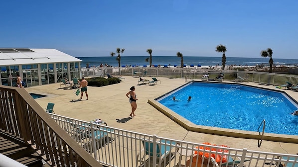 Un área de piscina con vista al océano, sillas de descanso y un edificio con grandes ventanales.