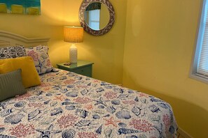 A bed with a patterned bedspread, a bedside lamp, a nightstand, and a mirror on the wall.
