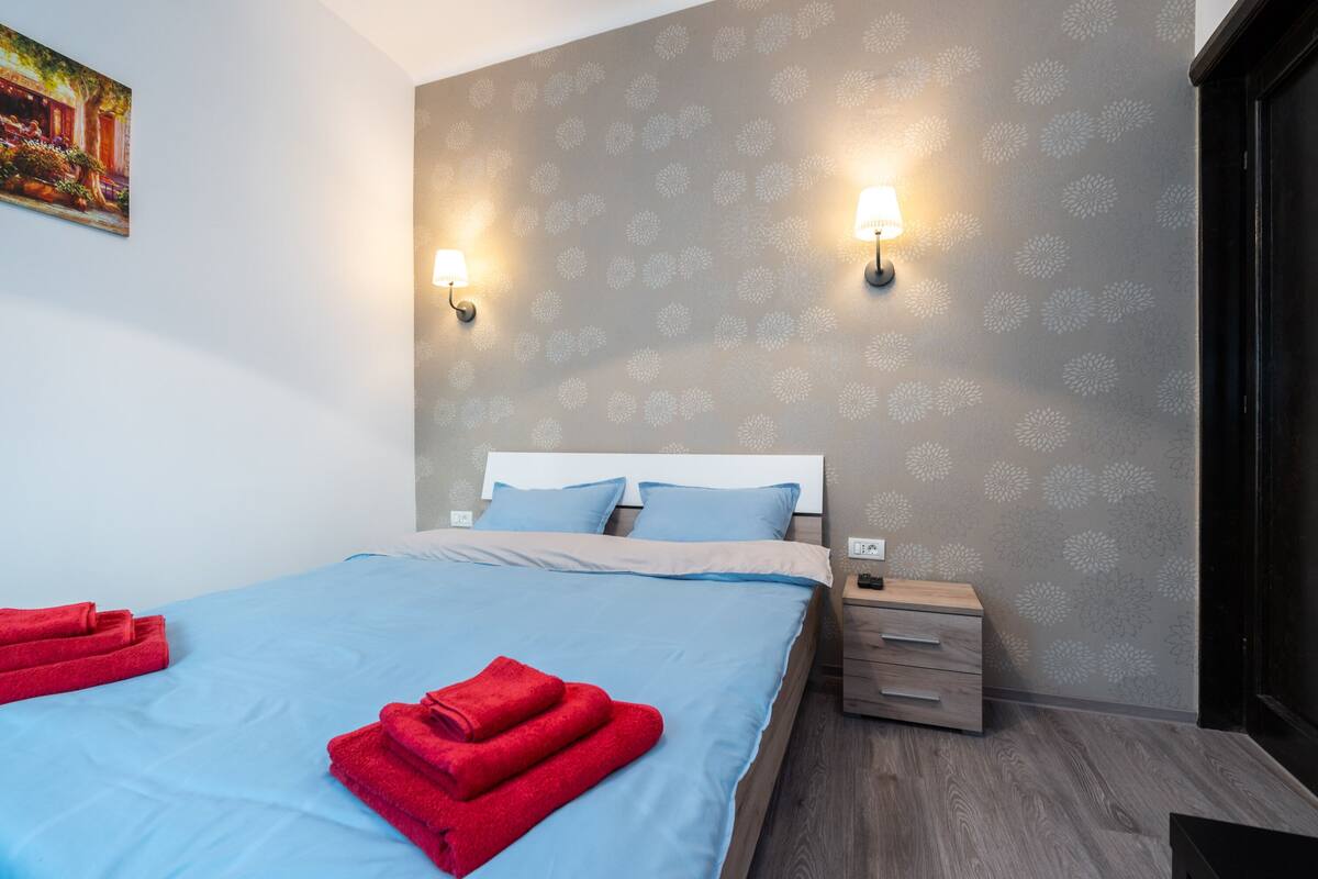 Ein Hotelzimmer mit einem Bett, zwei Wandlampen, einem Nachttisch und Holzboden.
