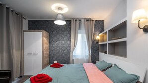 Ein modernes Hotelzimmer mit Bett, Kleiderschrank, Regalen und einem Fenster mit Vorhängen.