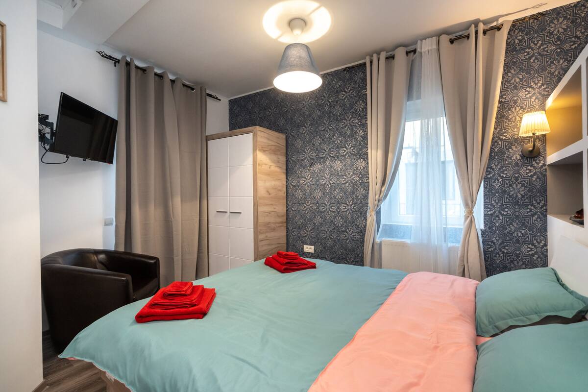 Ein Hotelzimmer mit Bett, Wandfernseher, Kleiderschrank und Schreibtisch mit Lampe.