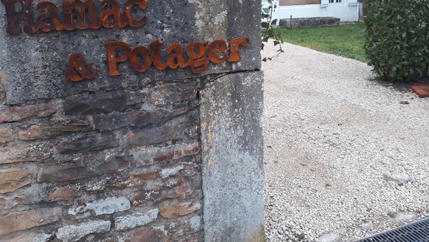 Una pared de piedra con un letrero de metal que dice "Hamac & Potager".