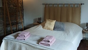 Una cama bien hecha con una colcha blanca texturizada, dos toallas dobladas y un cabecero de madera.