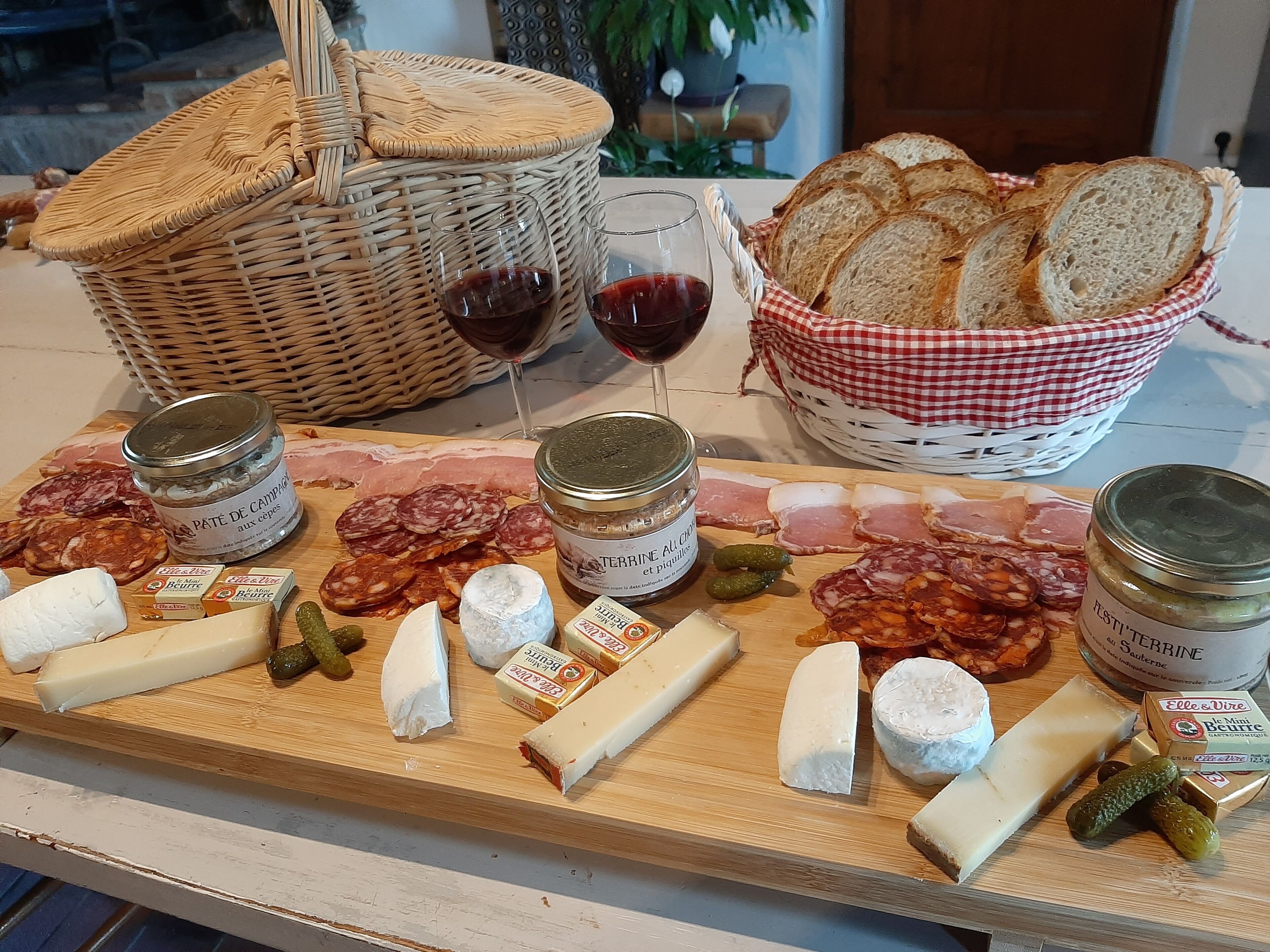 A charcuterie board with various cheeses, meats, and pickles, accompanied by glasses of red wine and a basket of bread.