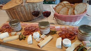 A charcuterie board with various cheeses, meats, and pickles, accompanied by glasses of red wine and a basket of bread.
