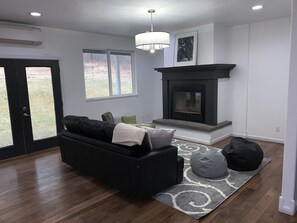 A modern living room with a black sofa, a fireplace, and a large window.
