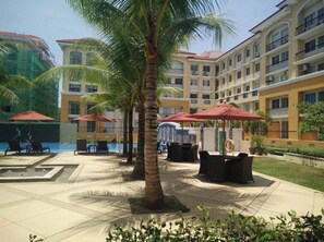 A hotel courtyard with palm trees, outdoor seating, and a pool.