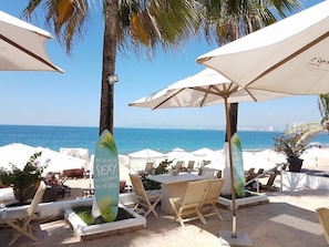 A beachside patio with white umbrellas, lounge chairs, and a table.