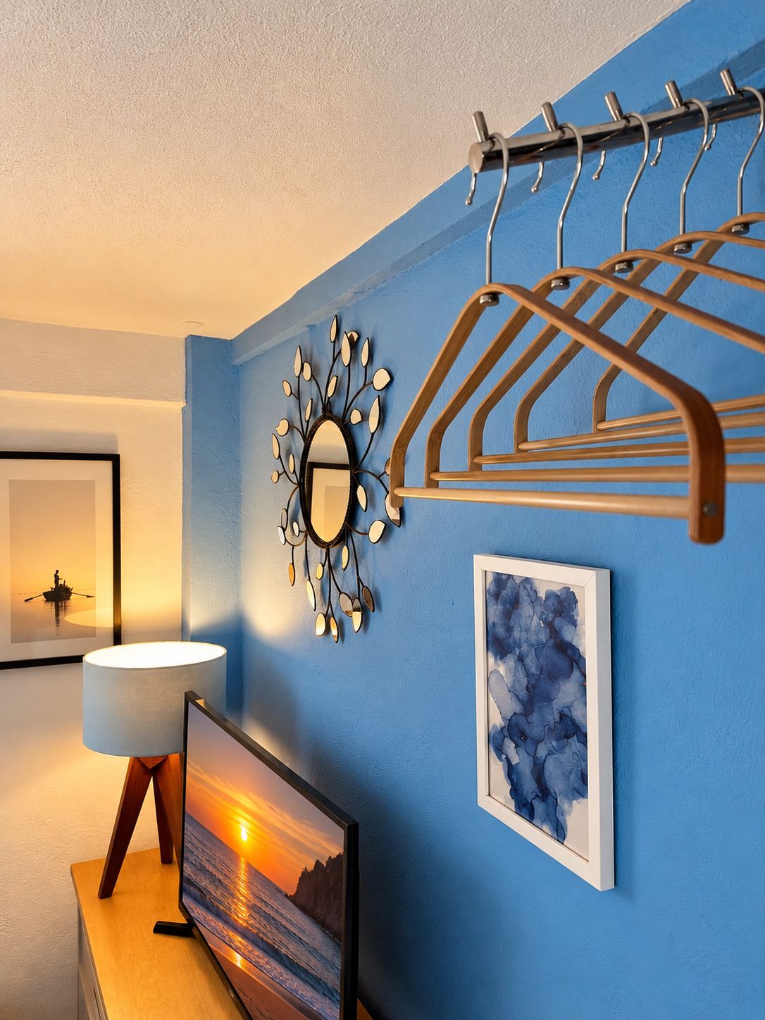 A room with a blue wall, a wall-mounted mirror, a framed picture, a lamp, and a television on a wooden stand.