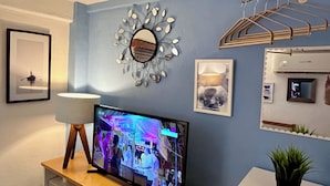 A living room with a TV, a wall-mounted mirror, a framed picture, and a small plant. - Le Petit Bonheur • Quiet • Rooftop • 3 min to Beach (5 de Diciembre)