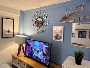 A living room with a TV, a wall-mounted mirror, a framed picture, and a small plant.