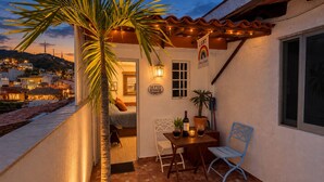 Un balcon avec un palmier, une table avec une bouteille et une chaise.