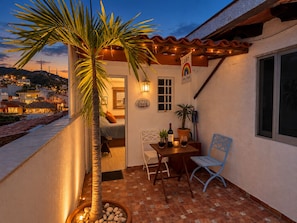 Un balcon avec un palmier, une table avec une bouteille et une chaise.