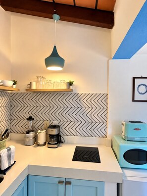 A kitchen with a modern design, featuring a herringbone patterned backsplash, a teal pendant light, and a vintage toaster.