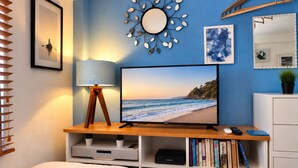 Une chambre à coucher avec un lit, un téléviseur posé sur un meuble en bois, une horloge murale et un miroir.