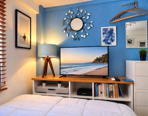 Une chambre à coucher avec un lit, un téléviseur posé sur un meuble en bois, une horloge murale et un miroir.