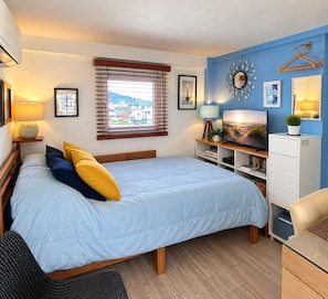 Une chambre à coucher avec un lit, des lampes de chevet, un téléviseur, une commode et une fenêtre avec des stores.