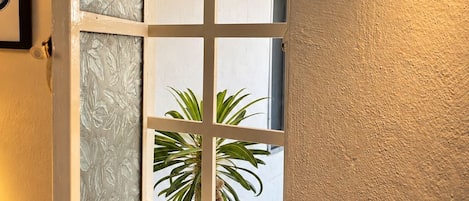Une pièce dotée d’une fenêtre avec des panneaux de verre dépoli, d’un plafond en bois et offrant une vue sur un palmier à l’extérieur.