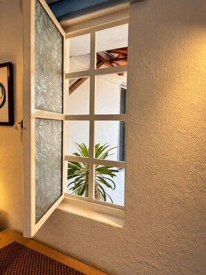A room with a window featuring frosted glass panels, a wooden ceiling, and a view of a palm tree outside. - Le Petit Bonheur • Quiet • Rooftop • 3 min to Beach (5 de Diciembre)