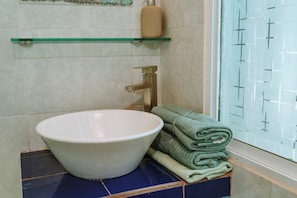 A bathroom with a white sink, a glass shelf, a towel, and a window with a patterned view.
