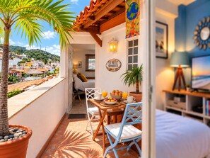 A balcony with a table set for breakfast, a bed, and a view of the town.