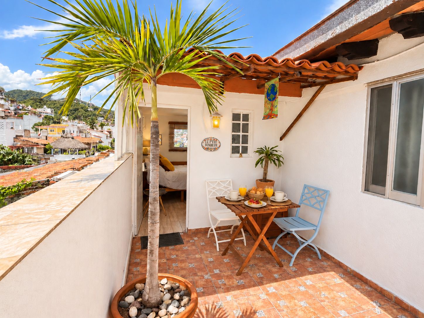 A small patio with a table, chairs, a potted plant, and a view of the surrounding neighborhood.