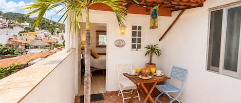 A small patio with a table, chairs, a potted plant, and a view of the surrounding neighborhood.