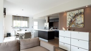 Una cucina moderna con isola centrale, un'area pranzo con tavolo e sedie, e un soggiorno con divano.
