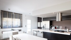 Una cucina moderna con un piano di lavoro bianco, elettrodomestici in acciaio inossidabile e una schiena di cucina nera. C'è un'area pranzo con un tavolo e sedie bianche.