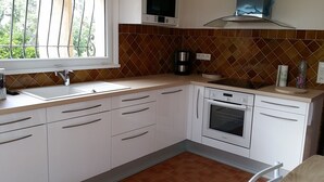 Una cocina con armarios blancos, un lavamanos de acero inoxidable, una cafetera y un microondas.