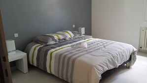 Una cama bien hecha con ropa de cama a rayas en una habitación con pared gris y mesitas de noche blancas.