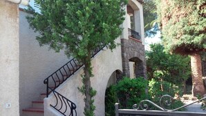 Una escalera con barandilla de metal, un arco de piedra y un árbol con follaje verde.
