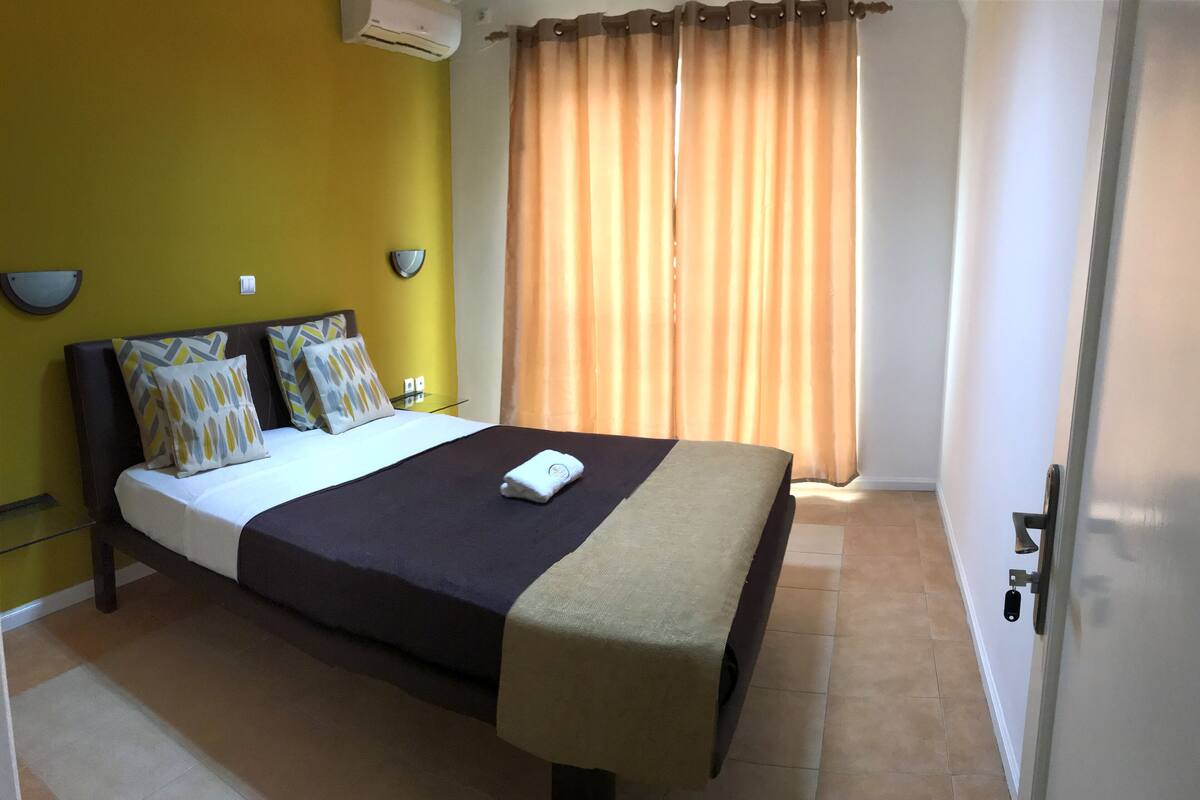 A hotel room with a bed, a bedside table, a lamp, and a window with curtains.