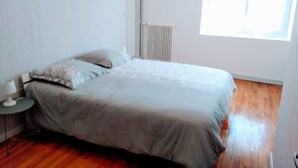 Un dormitorio con cama, una mesita, un radiador y una ventana.