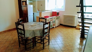 Una cocina con una mesa de comedor, sillas, un refrigerador, un microondas y una ventana con cortinas.