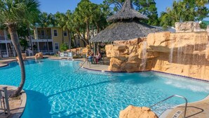 A swimming pool with clear blue water, surrounded by palm trees and a thatched-roof structure.