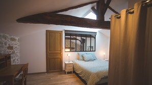 A bedroom with a wooden floor, a bed with patterned bedding, a nightstand with a lamp, a stone wall, and a wooden door. - Exceptional house with heated pool - 8 people (Saint-Georges-de-Pointindoux)