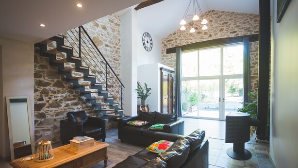 A spacious living area with a stone staircase, leather sofas, a wooden coffee table, and a large window providing natural light. - Exceptional house with heated pool - 8 people (Saint-Georges-de-Pointindoux)