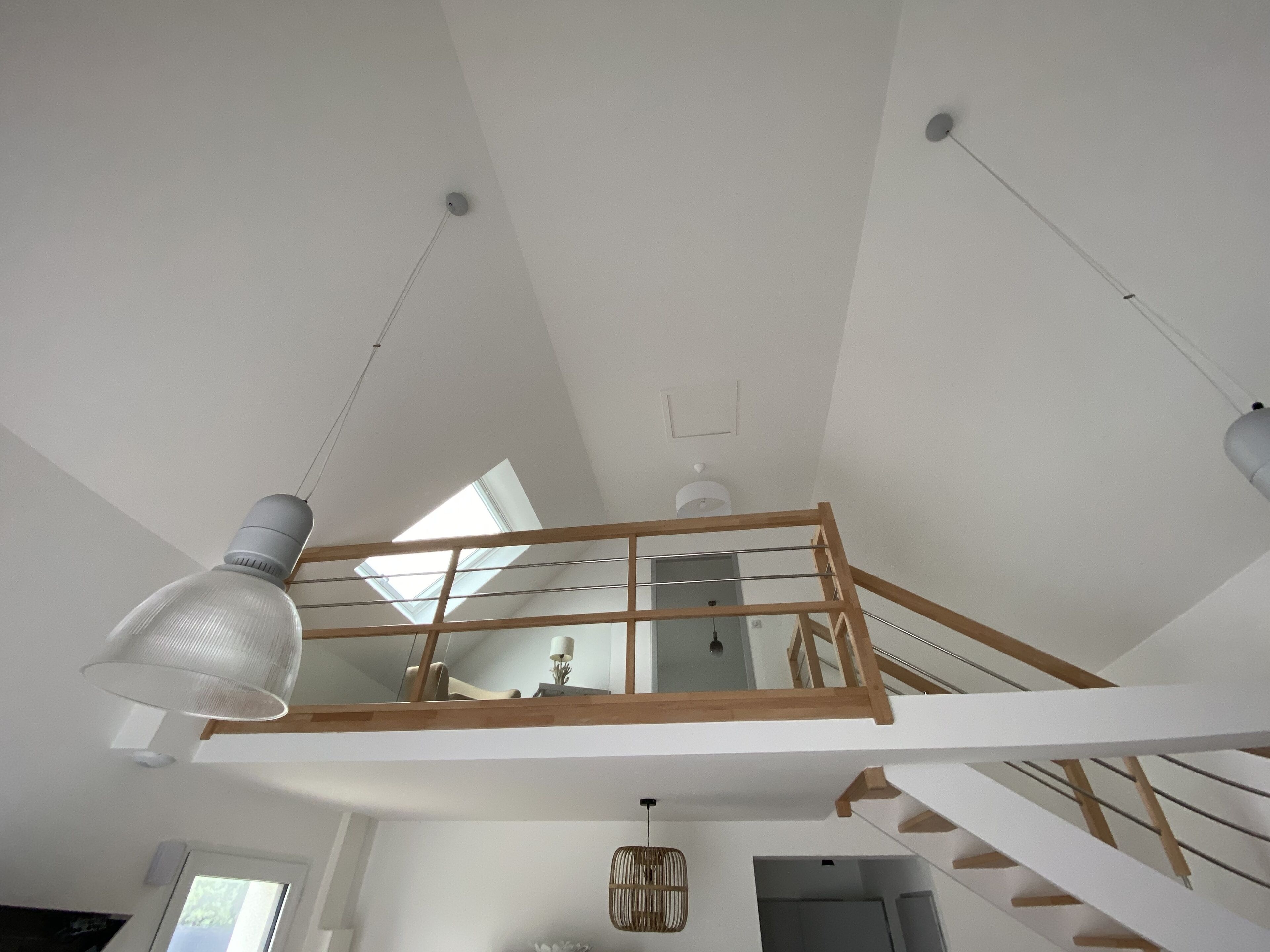 A high-ceilinged room with skylights, a wooden staircase, and a hanging light fixture.