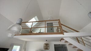 Um quarto com pé-direito alto, claraboias, escada de madeira e luminária suspensa.
