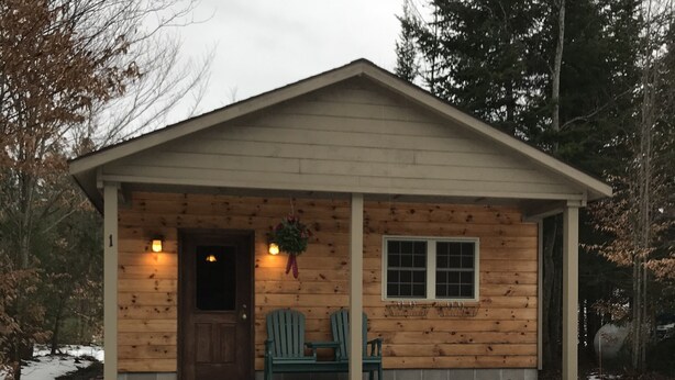 Eine kleine Holzhütte mit Veranda, Tür und Fenster.