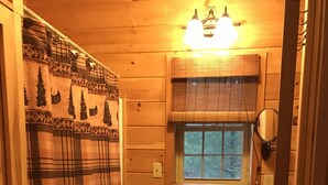 Ein Badezimmer mit Holzvertäfelung, einem weißen Waschbecken, einem Fenster mit Jalousien und einem Karo-Duschvorhang.