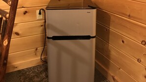 Ein kompakter Kühlschrank in einer Ecke mit Holzwänden und Teppichboden.
