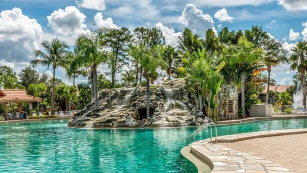 Ein Pool mit Felsformation, umgeben von Palmen und einer Steindeck.