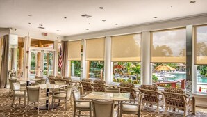Eine Hotlelloge mit Blick auf einen Pool, ausgestattet mit einem gemusterten Teppich, Korbmöbeln und großen Fenstern.