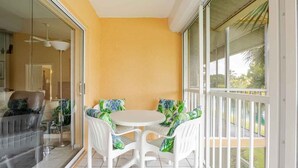 Ein Balkon mit einem weißen Tisch und Stühlen, eine Glastür, die zu einem Zimmer führt, und Blick ins Grüne.