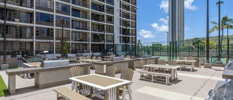 A rooftop patio with outdoor seating, a barbecue area, and a view of a high-rise building.