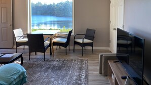 Une pièce dotée d’une grande fenêtre donnant sur un lac, d’un téléviseur et d’un coin repas avec des chaises et une table.