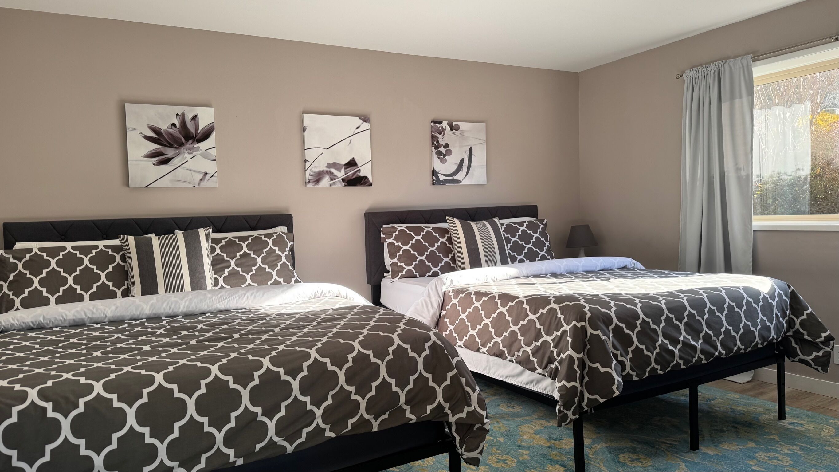 A bedroom with two beds, a window with curtains, and three wall-mounted artworks.